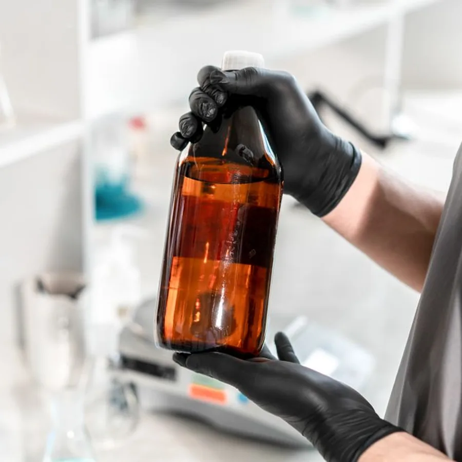 Gloved hands holding an amber bottle in a lab